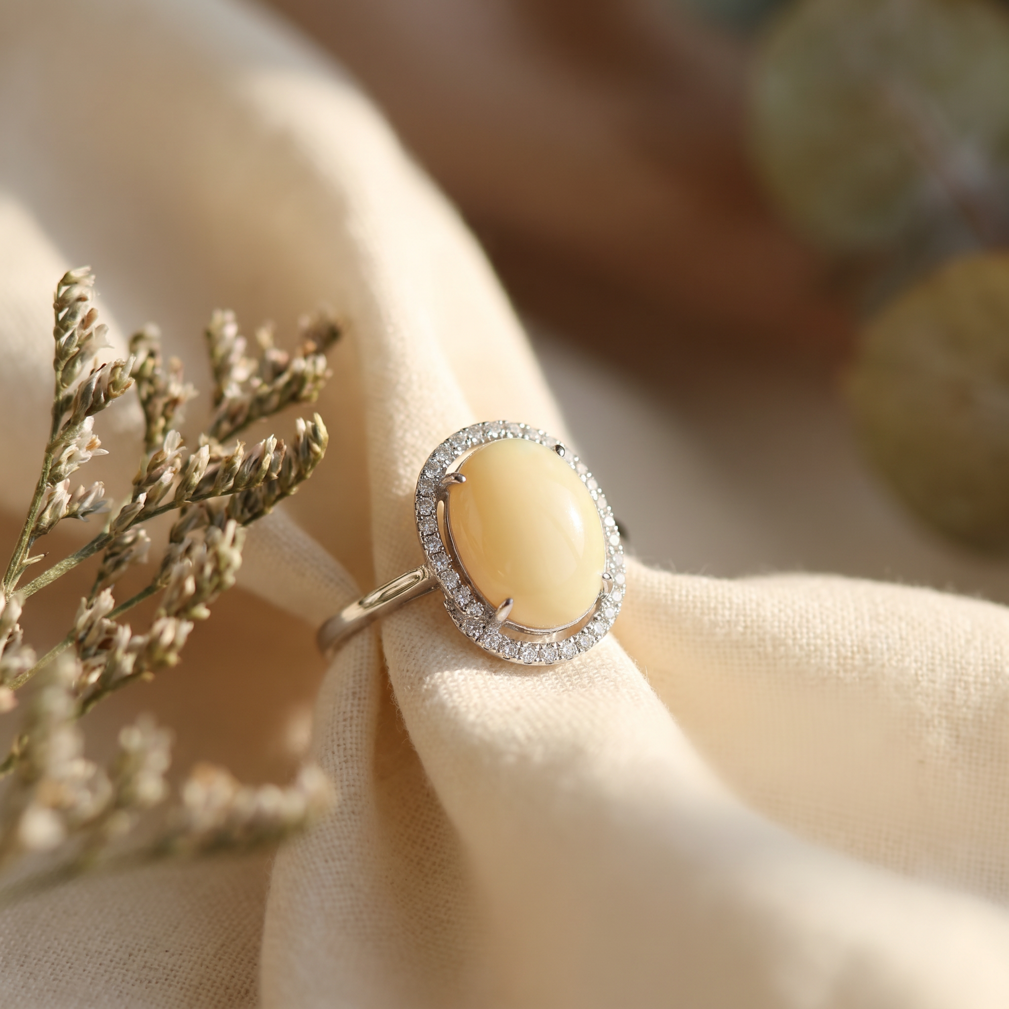 Oval opal halo cocktail ring in 18K white gold on warm linen — the Rings collection