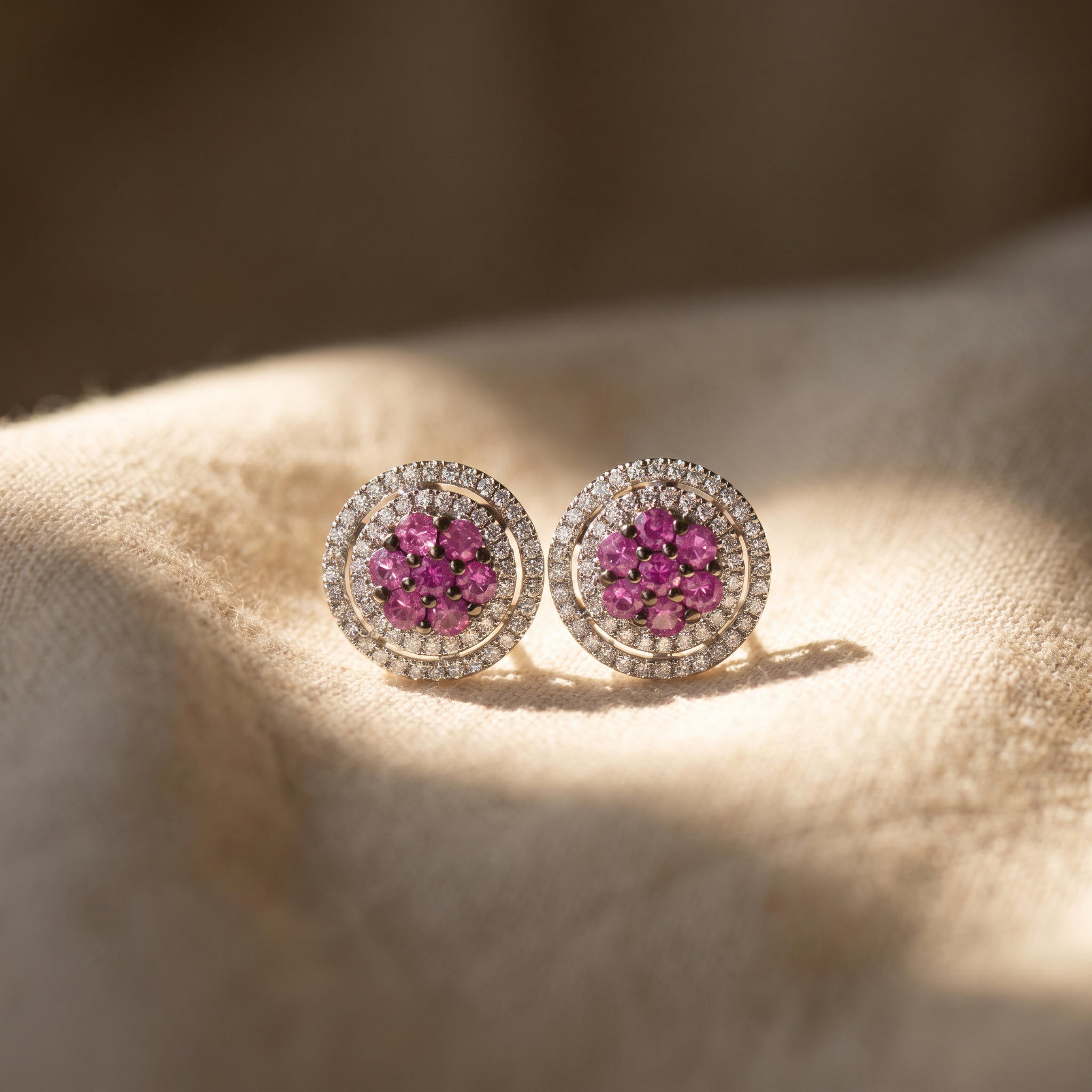 Pink sapphire double-halo cluster earrings in 18K white gold, editorial scene on warm linen