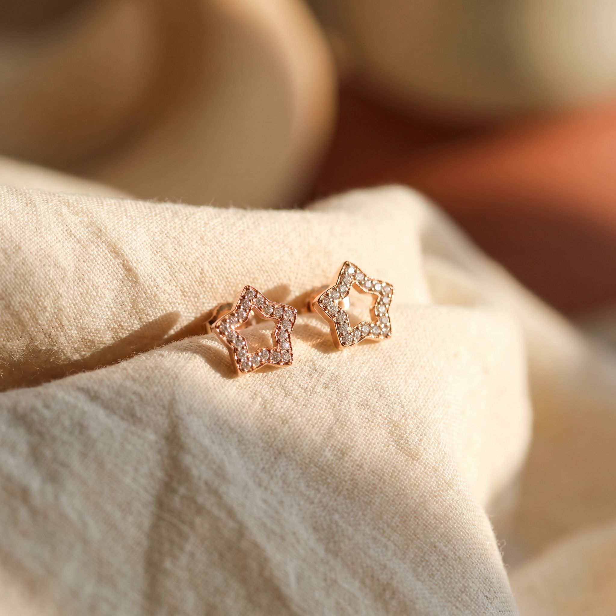 Open-star diamond stud earrings in 18K rose gold, editorial scene on warm linen
