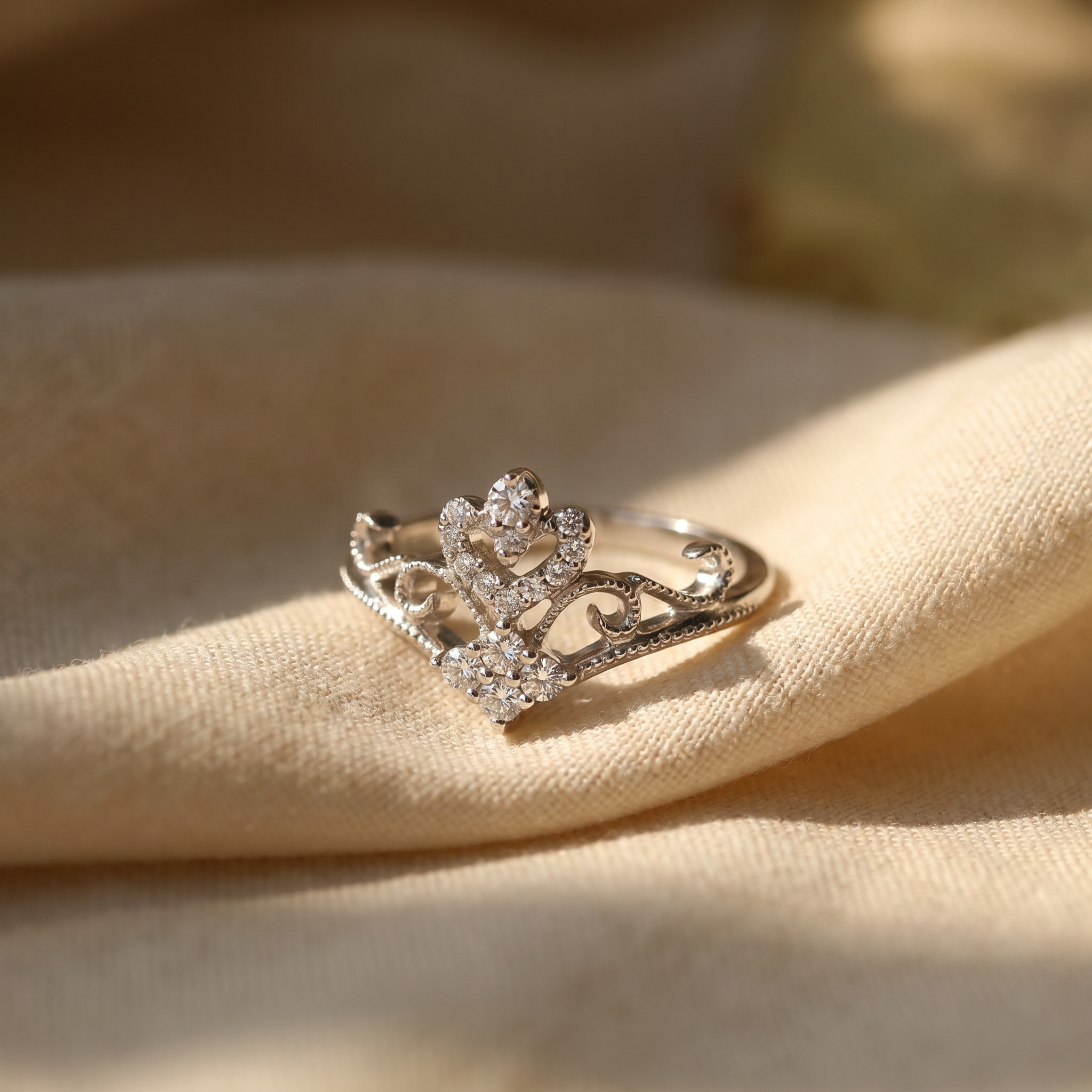 Diamond crown cocktail ring in 18K white gold, editorial scene on warm linen