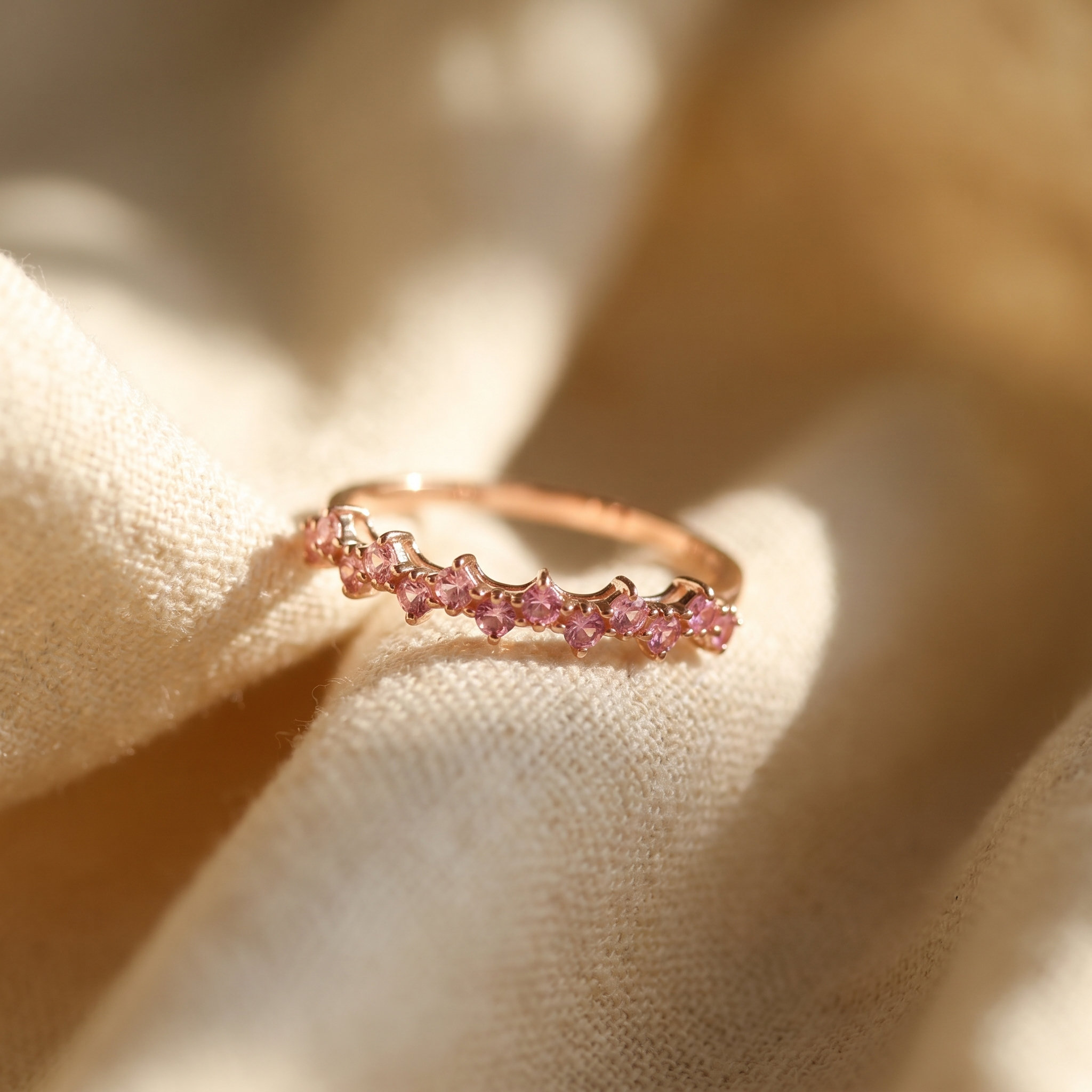 Pink sapphire curved stacking ring in 18K rose gold, editorial scene on warm linen