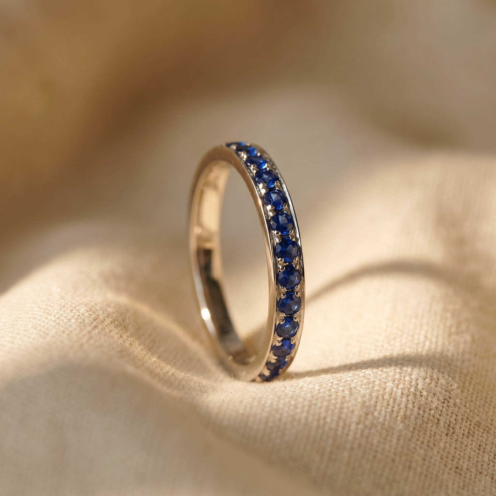 Royal blue sapphire eternity ring in 18K white gold, editorial scene on warm linen