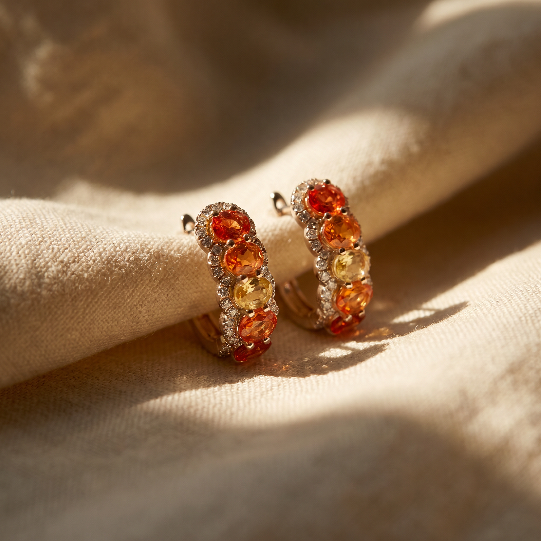 Mandarin orange sapphire hoop earrings in 18K white gold, editorial scene on warm linen