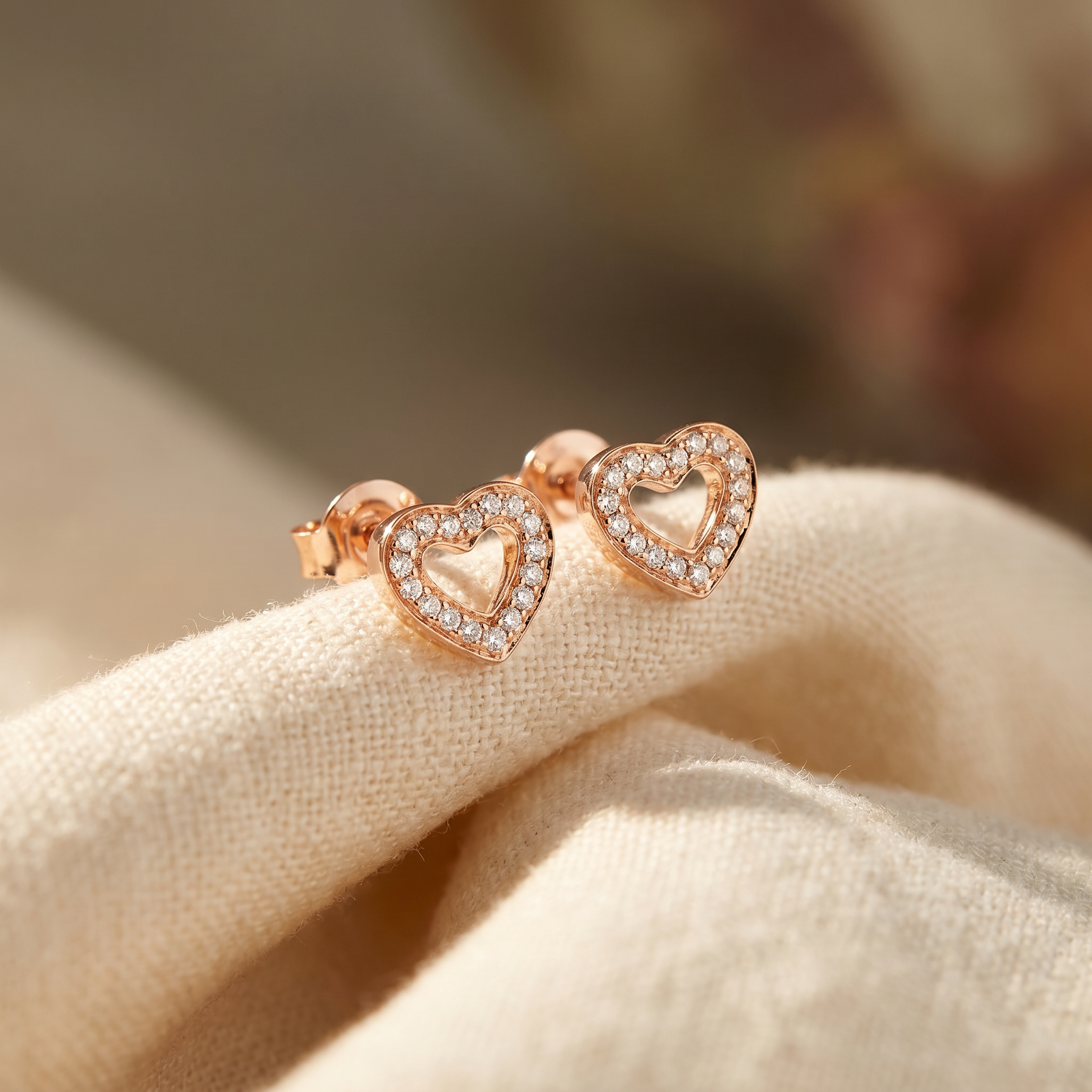 Open-heart diamond stud earrings in 18K rose gold, editorial scene on warm linen