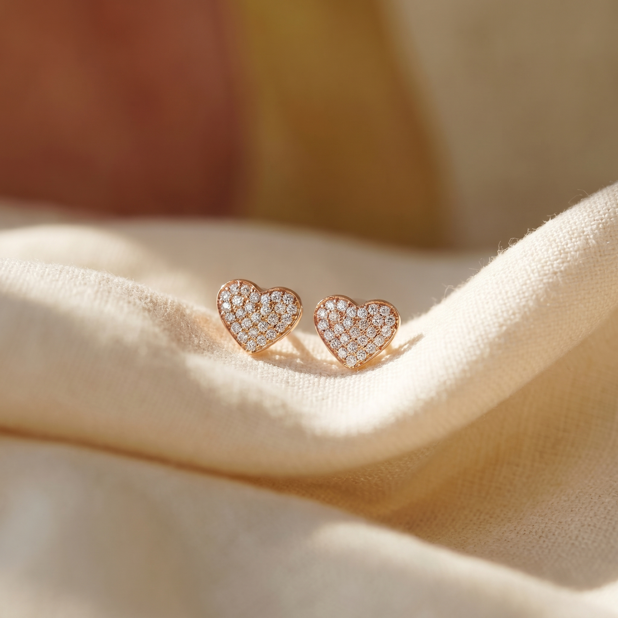 Pavé diamond heart stud earrings in 18K rose gold, editorial scene on warm linen
