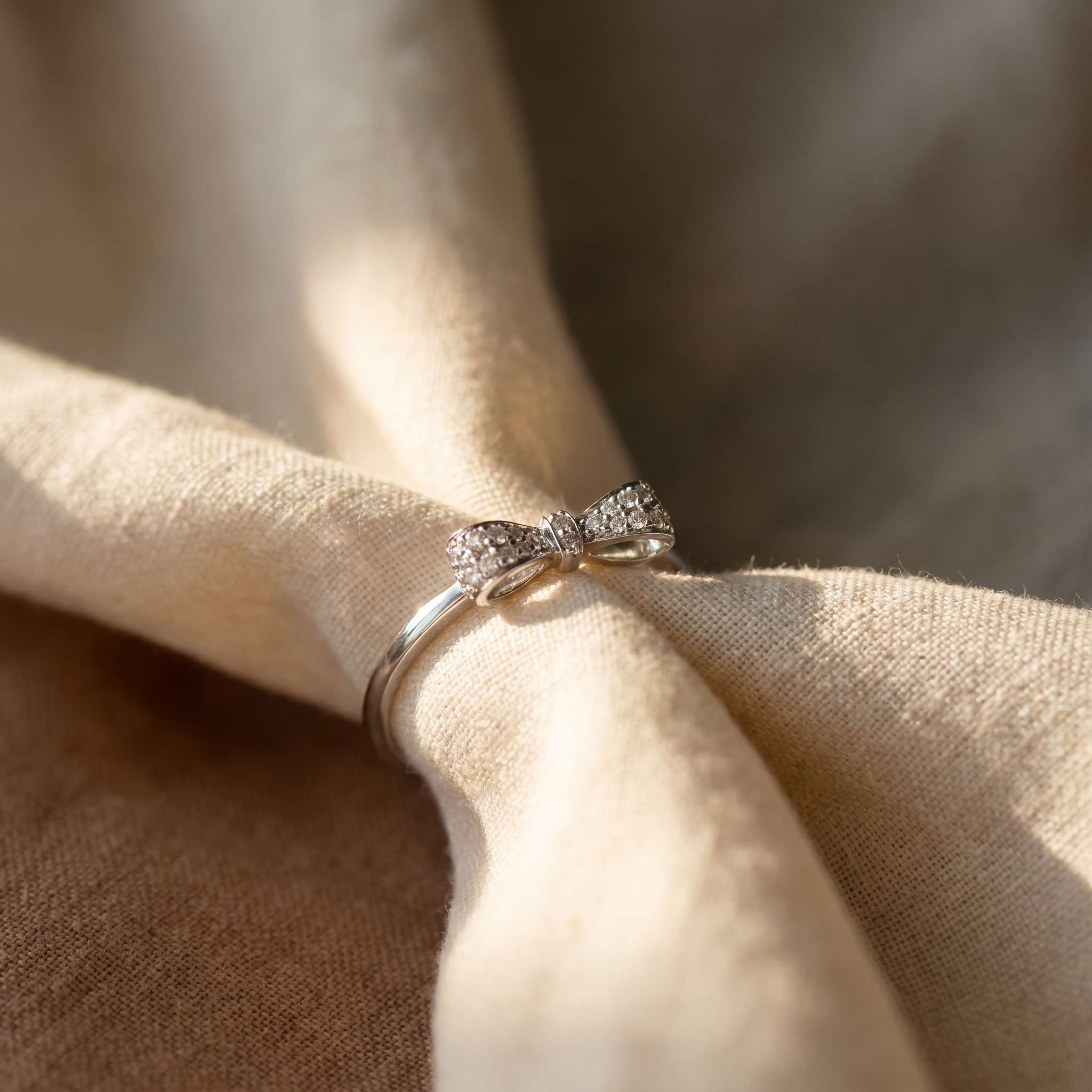 Diamond pavé bow ring in 18K white gold, editorial scene on warm linen