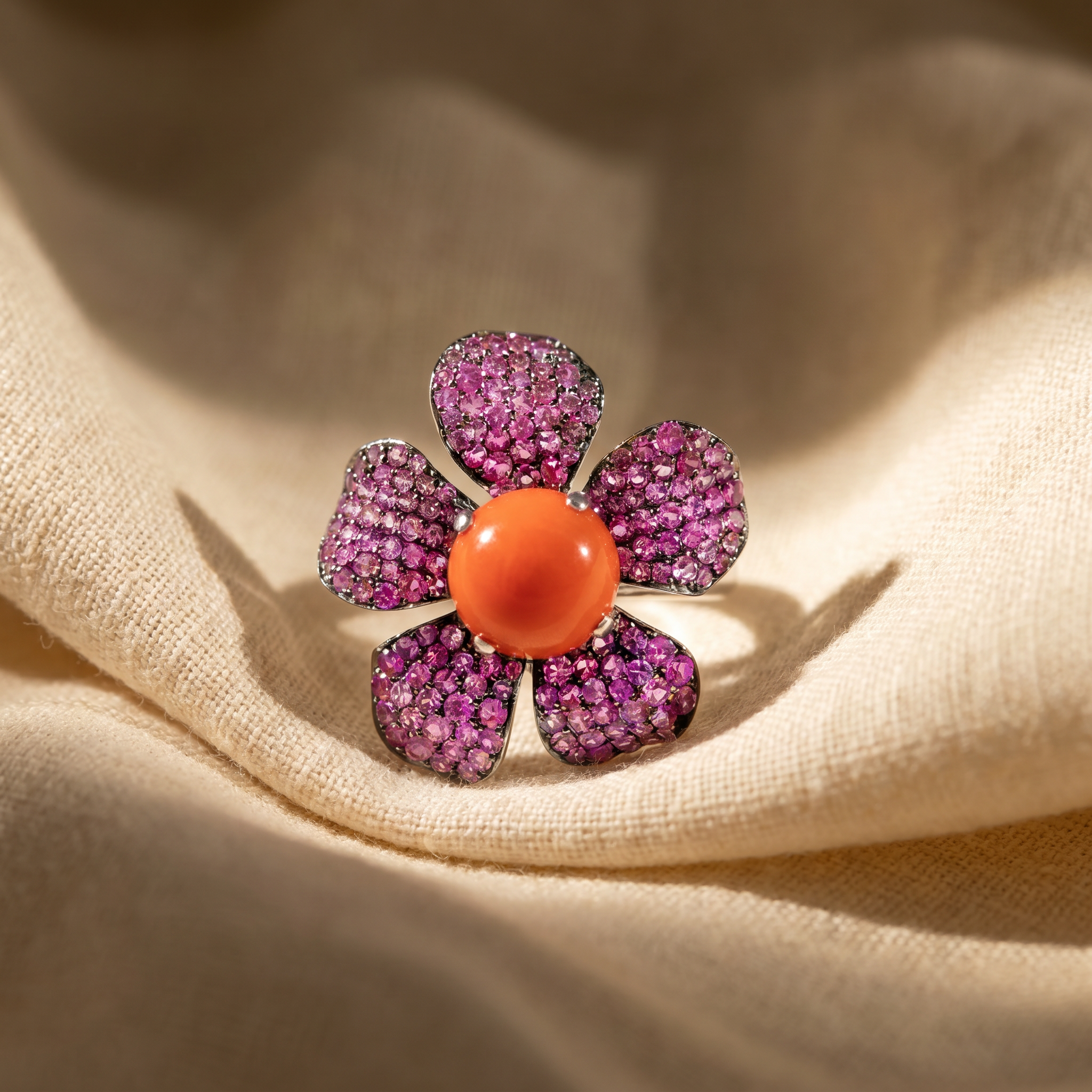 Coral cabochon flower cocktail ring in 18K white gold, editorial scene on warm linen