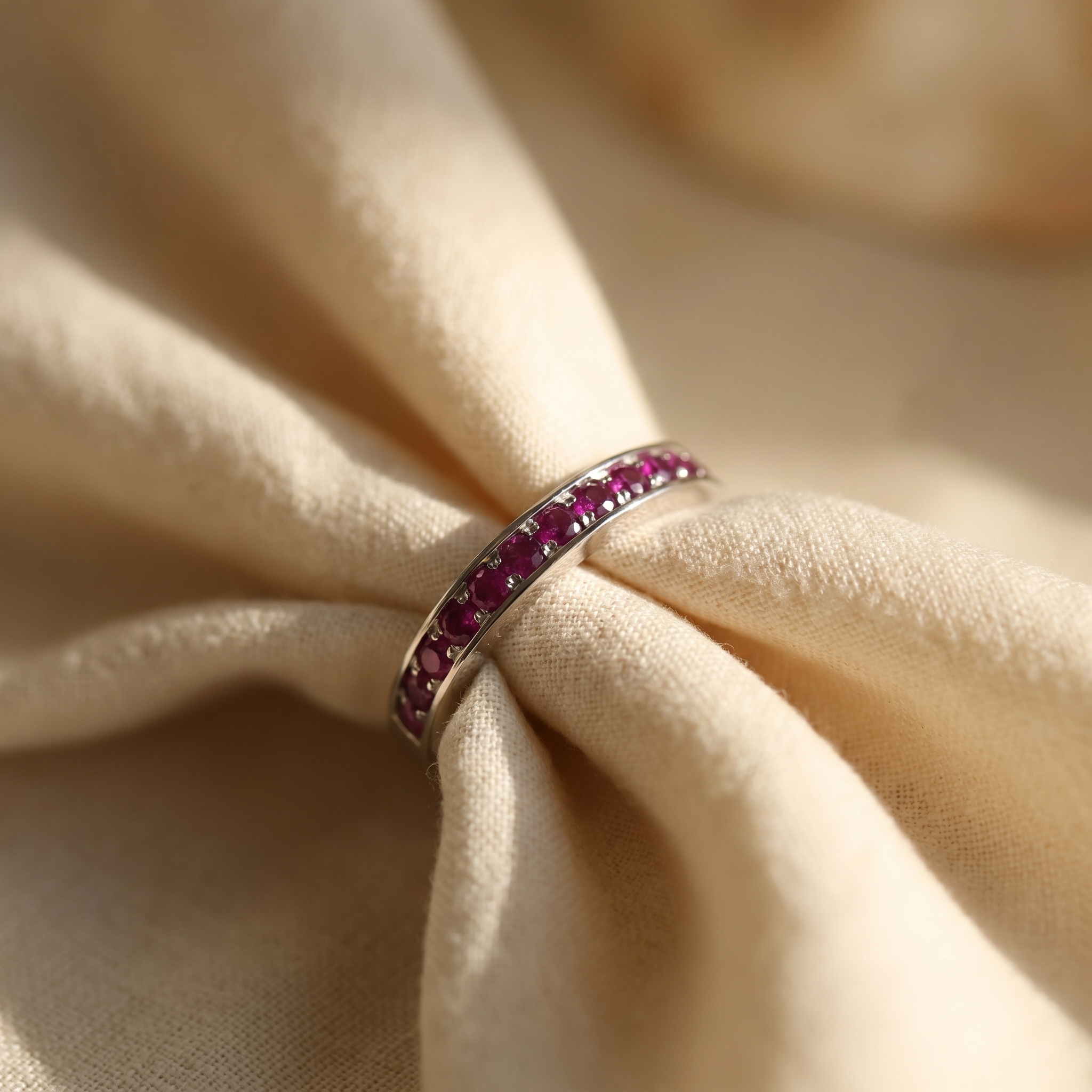 Purplish-red ruby eternity ring in 18K white gold, editorial scene on warm linen